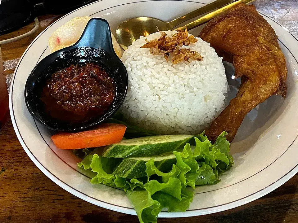 Ayam goreng penyet dengan nasi, sambal dalam cobek kecil, dan lalapan selada, tomat, serta timun